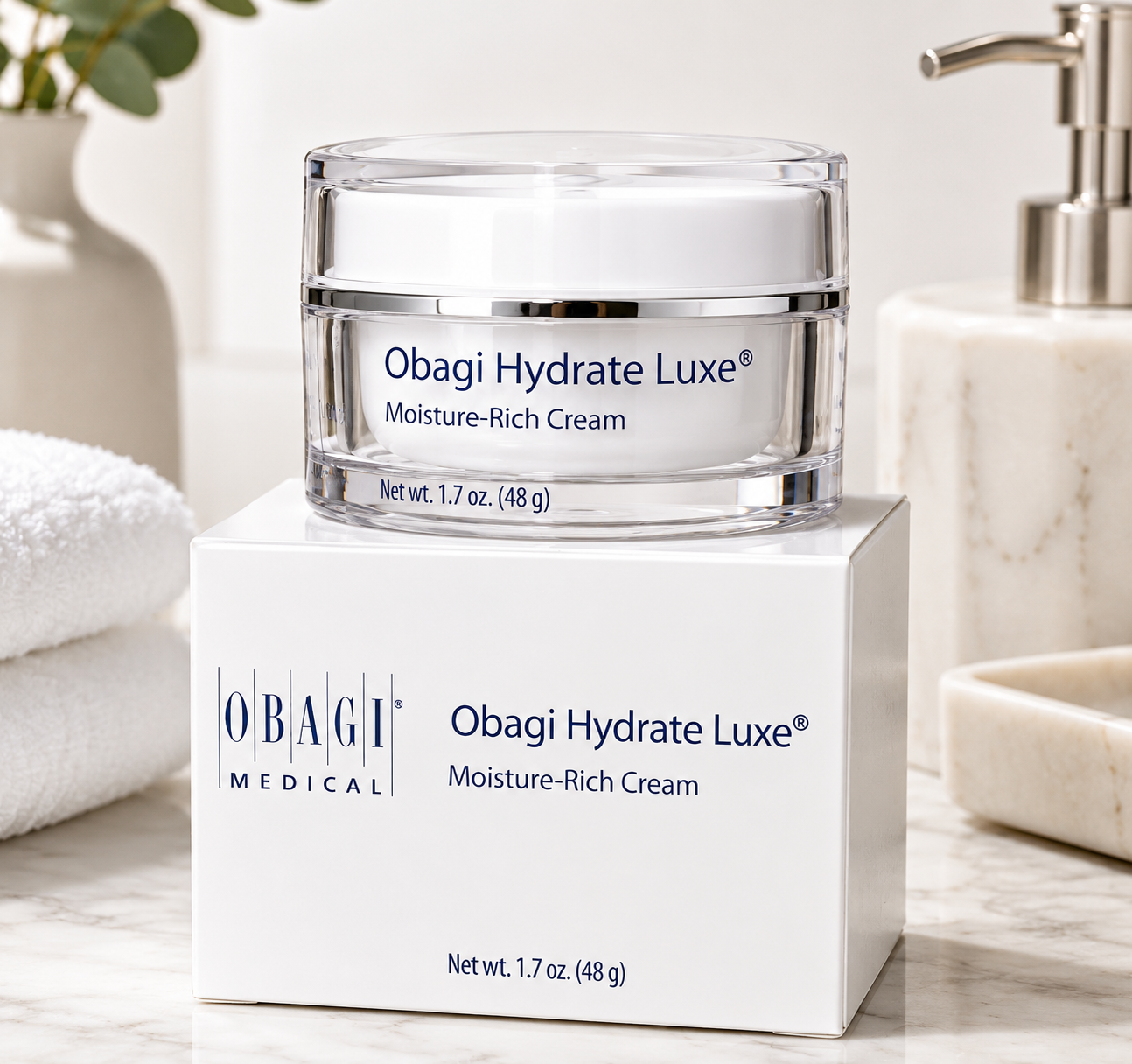 Obagi Hydrate Luxe Moisture-Rich Cream jar on a white box with a bathroom setting.